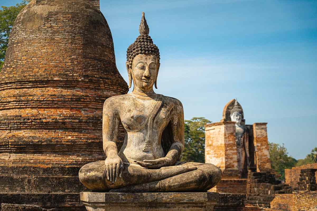Statue du Bouddha assise en lotus, temple en briques rouges, ciel clair